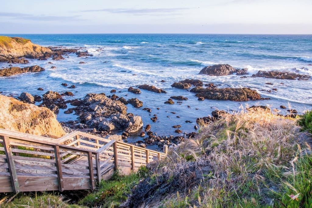 Une vue sur la côte, avec un paysage rocheux, un escalier en bois et un ciel dégagé.