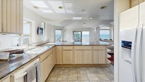 A modern kitchen with a large island, built-in appliances, and a view of the sea.