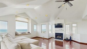 A spacious living room with a large sofa, a fireplace, and a ceiling fan.