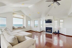 A spacious living room with a large sofa, a fireplace, and a ceiling fan. - Lovely House w/Beautiful Ocean Views, Grill & Jetted Tub - Walk  to Beach & Town (Cayucos)