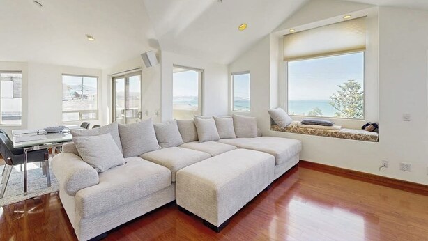 A modern living room with a sectional sofa, large windows, and a dining area.