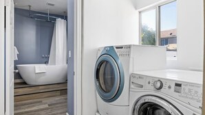 Un lavadero con lavadora de carga frontal, una bañera y una ventana que aporta luz natural.