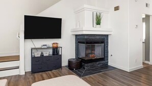 Una sala de estar moderna con chimenea, televisor de pantalla plana, piso de madera oscura y mueble de entretenimiento negro.