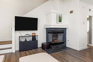 Ein modernes Wohnzimmer mit Kamin, Flachbildfernseher, dunklem Holzboden und einer schwarzen Unterhaltungsanlage.