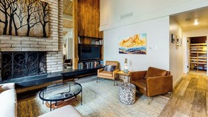 Una sala de estar con chimenea, televisor, estantería y un cuadro en la pared.