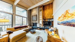 Una sala de estar moderna con chimenea, ventanas amplias y un cuadro en la pared.