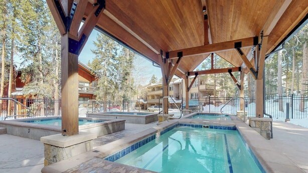 Zona de piscina exterior con vigas de madera, una sección cubierta y vistas de edificios circundantes.