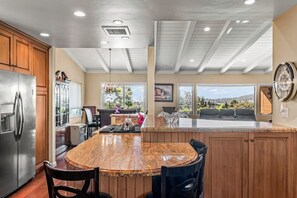 Eine Küche mit einer Granit Arbeitsplatte, Holzschränken, einem Edelstahlkühlschrank und einem Essbereich mit Stühlen.