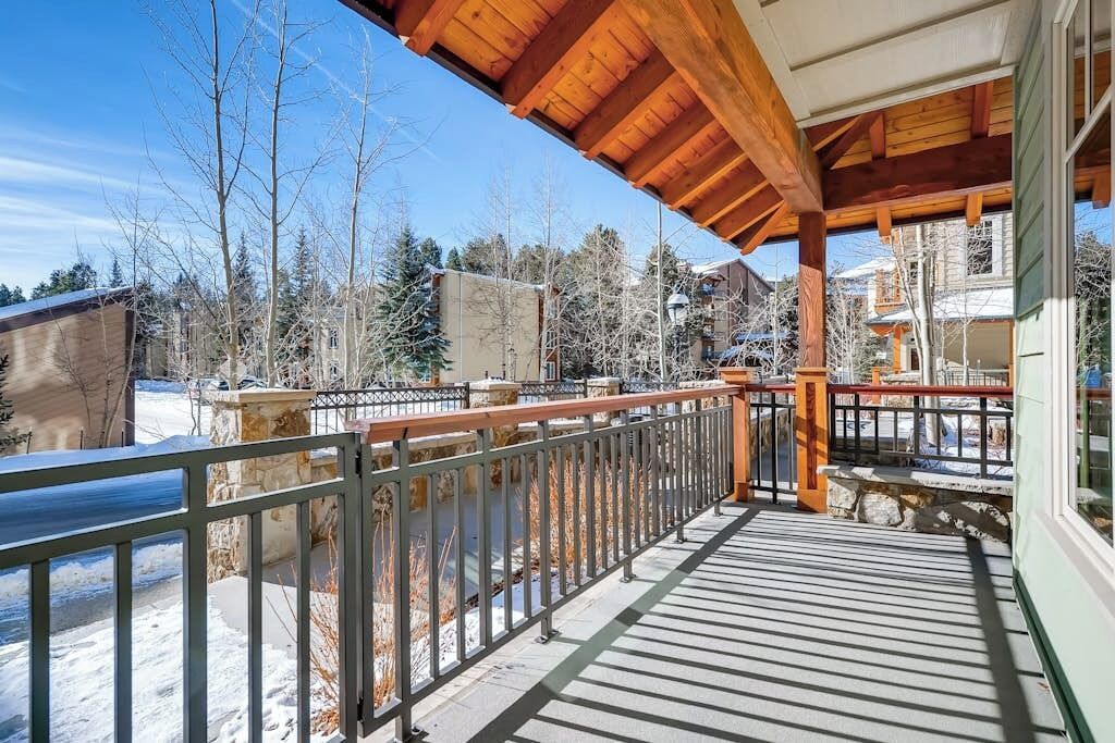 A wooden deck with a metal railing, a stone wall, and a clear view of a snowy landscape.