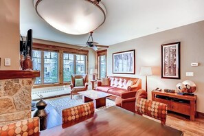 Ein geräumiges Wohnzimmer mit Kamin, großem Fenster, Deckenventilator und Couchtisch aus Holz.