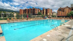 Una piscina con sillones de descanso, una torre del reloj y edificios de varios pisos al fondo.
