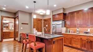 Una cocina con armarios de madera, un refrigerador de acero inoxidable, un fregadero y una zona de bar con taburetes.