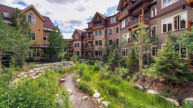 Un edificio de varios pisos con balcones, un sendero de piedra y vegetación circundante.