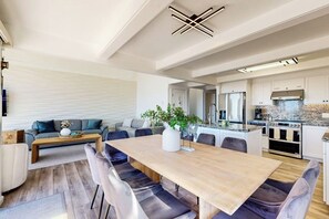 A modern kitchen with a central island, built-in appliances, and a dining area with a wooden table and chairs. - Beachfront home with heated pool, hot tub, sports courts, amazing views, & WFH (Moss Landing)