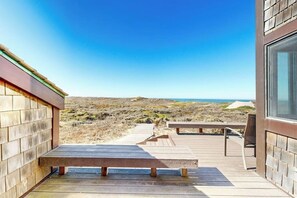 A wooden deck with a bench and table, overlooking a coastal landscape. - Beachfront home with heated pool, hot tub, sports courts, amazing views, & WFH (Moss Landing)