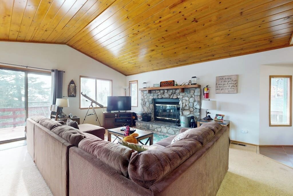 A cozy living room with a stone fireplace, wooden ceiling, and a large sofa.