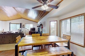 A dining area with a wooden table and chairs, a ceiling fan, and a television in the background. - Cheery cabin with gas grill, patio, deck, outdoor space, & near lake (Lake Arrowhead)