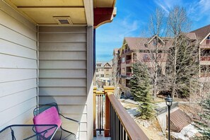 A balcony with a chair, a railing, and a view of multi-story buildings and trees. - Luxury condo with balcony, pool, hot tubs & gym - walk to lifts/downtown (Breckenridge)