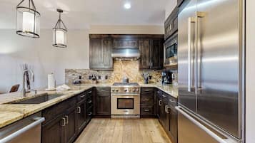 Una cocina moderna con armarios de madera oscura, electrodomésticos de acero inoxidable, un salpicadero de mármol e iluminación colgante.