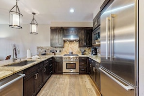 A modern kitchen with dark wood cabinets, stainless steel appliances, a marble backsplash, and pendant lighting. - Luxury condo with balcony, pool, hot tubs & gym - walk to lifts/downtown (Breckenridge)
