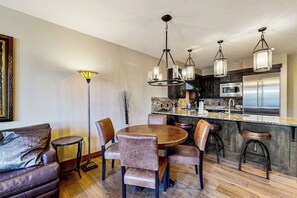 A modern kitchen with a central island, pendant lighting, and a dining area with a round table and chairs. - Luxury condo with balcony, pool, hot tubs & gym - walk to lifts/downtown (Breckenridge)