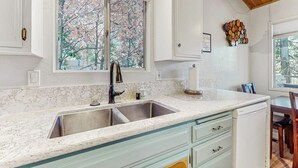 A kitchen with a double sink, a window with a view of trees, and a wooden ceiling. - Mountainside Retreat w/ Fireplace, BBQ & Furnished Deck - Near Village (Lake Arrowhead)