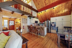 Ein rustikales Blockhaus-Interieur mit Holzbalkendecke, einer Küche mit Barhocker und einem Essbereich.