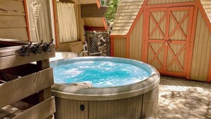 A hot tub in a wooden outdoor setting with a wooden fence and a red gate in the background. - Cabin w/ Loft, hot tub, Fireplace, game room & Private lake trail access (Lake Arrowhead)