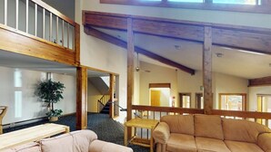 A spacious interior with a high ceiling, wooden beams, a staircase, a sofa, a small table, and a potted plant. - Conveniently Located Condo with Shared Pool, Hot Tub - Walk to Slopes (Keystone)