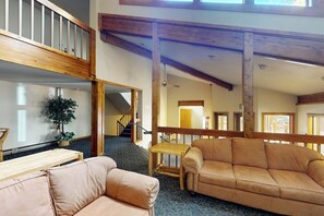 A spacious interior with a high ceiling, wooden beams, a staircase, a sofa, a small table, and a potted plant. - Conveniently Located Condo with Shared Pool, Hot Tub - Walk to Slopes (Keystone)