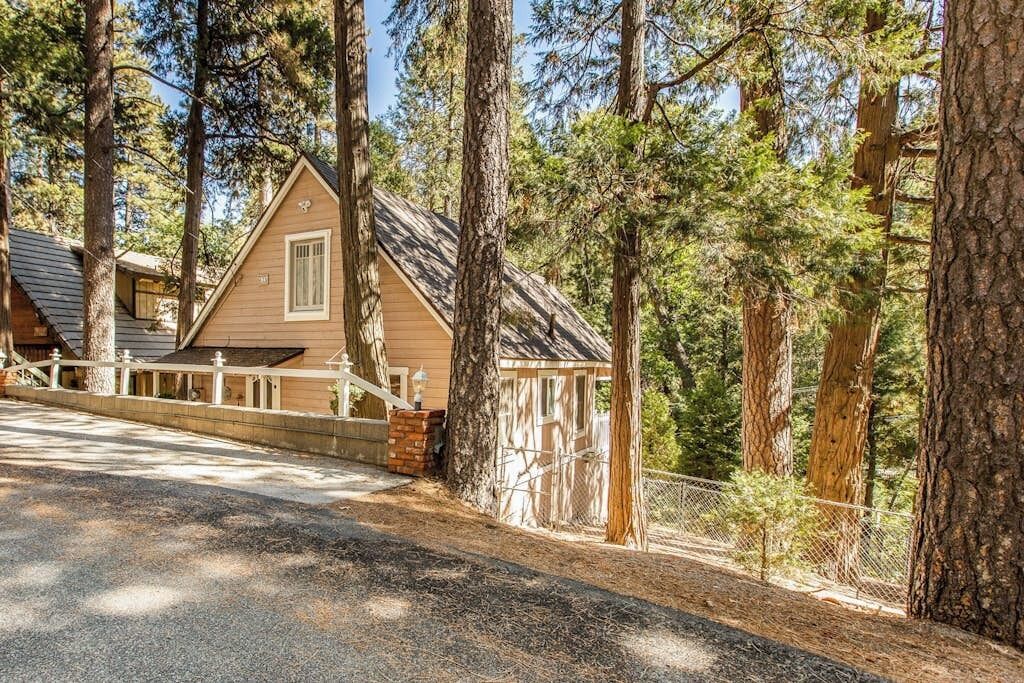Une cabane dotée d’un toit en pente, entourée de grands arbres, et une allée pavée menant à l’entrée.
