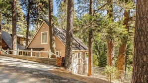 A cabin with a sloped roof, surrounded by tall trees, and a paved driveway leading to the entrance. - Near Lake Arrowhead Village with loft , Deck & Lake Access Card (Lake Arrowhead)