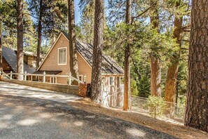 A cabin with a sloped roof, surrounded by tall trees, and a paved driveway leading to the entrance. - Near Lake Arrowhead Village with loft , Deck & Lake Access Card (Lake Arrowhead)