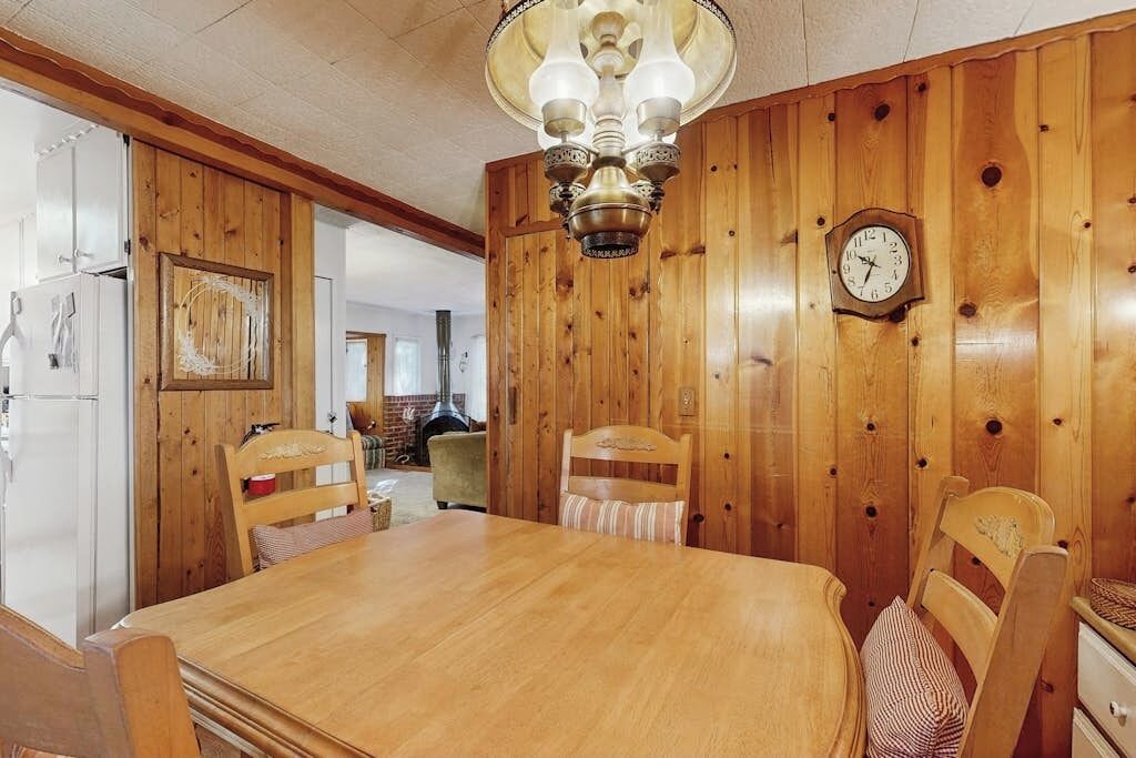 A wooden-paneled dining room with a wooden table and chairs, a chandelier, and a wall clock.
