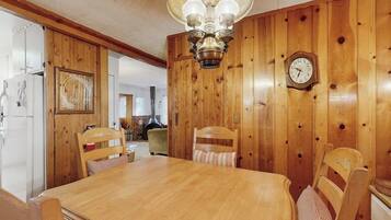 A wooden-paneled dining room with a wooden table and chairs, a chandelier, and a wall clock.