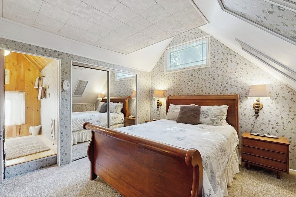 Une chambre à coucher avec un lit en bois, un miroir, une table de chevet et une fenêtre.
