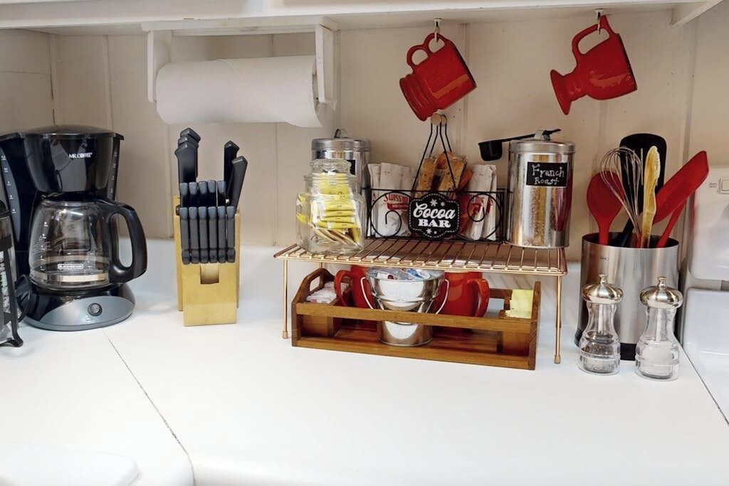 A kitchen counter with a coffee maker, knife block, spice rack, and hanging mugs.