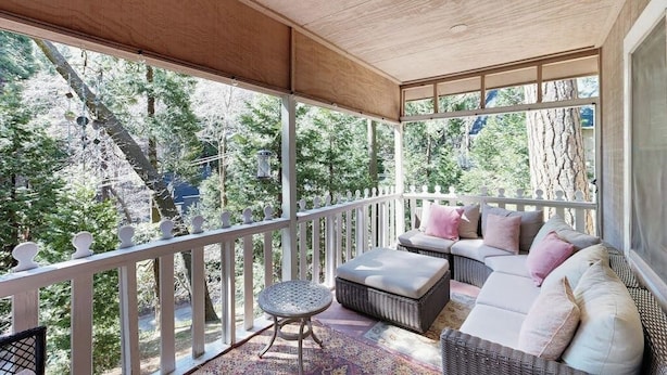 A covered porch with a white railing, wicker furniture, and a view of trees. - Near Lake Arrowhead Village with loft , Deck & Lake Access Card (Lake Arrowhead)