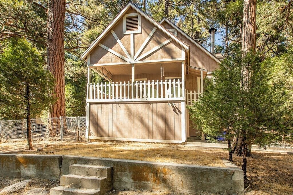 A two-story wooden cabin with a white picket fence, surrounded by trees.