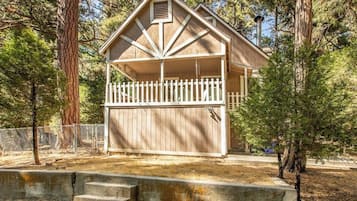 A two-story wooden cabin with a white picket fence, surrounded by trees.
