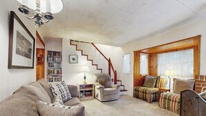 A living room with a sofa, armchair, and ottoman, a staircase, and a bookshelf. - Near Lake Arrowhead Village with loft , Deck & Lake Access Card (Lake Arrowhead)