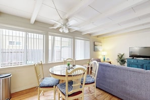 Ein Wohnzimmer mit rundem Tisch, Stühlen, einer Couch, einem Deckenventilator, einem Fernseher und einem Fenster mit Jalousien.