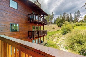 Eine Holzdiele mit Balkon, einem Steinkamin und Blick auf einen bewaldeten Hang.