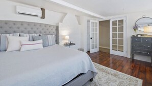 Quarto com cama grande, mesa de cabeceira, penteadeira e porta branca que dá para outro cômodo.