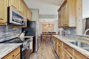 Eine Küche mit Holzausstattung, einer Granit Arbeitsplatte, einem Edelstahl-Spülbecken und einem Essbereich mit einer Kristallleuchtre.'