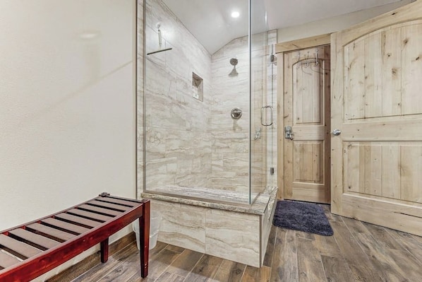Eine Dusche mit Glastüren, eine Holzbank und eine Holztür.