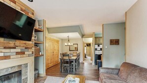 A living room with a fireplace, a television, a sofa, a dining area with a table and chairs, and a kitchen in the background. - Charming Townhouse with WiFi, Wood-Burning Fireplace, and Private Washer/Dryer (Breckenridge)