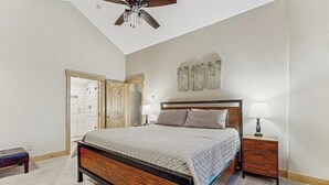 A bedroom with a bed, wooden headboard, two bedside tables with lamps, a ceiling fan, and a door leading to another room. - Charming Townhouse with WiFi, Wood-Burning Fireplace, and Private Washer/Dryer (Breckenridge)