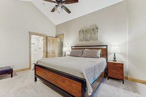 Ein Schlafzimmer mit einem Bett, einem Holz-Kopfteil, zwei Nachttischen mit Lampen, einem Deckenventilator und einer Tür zu einem anderen Raum.