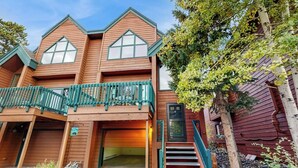 A two-story wooden building with a balcony, a front door, and a staircase leading to the entrance. - Charming Townhouse with WiFi, Wood-Burning Fireplace, and Private Washer/Dryer (Breckenridge)